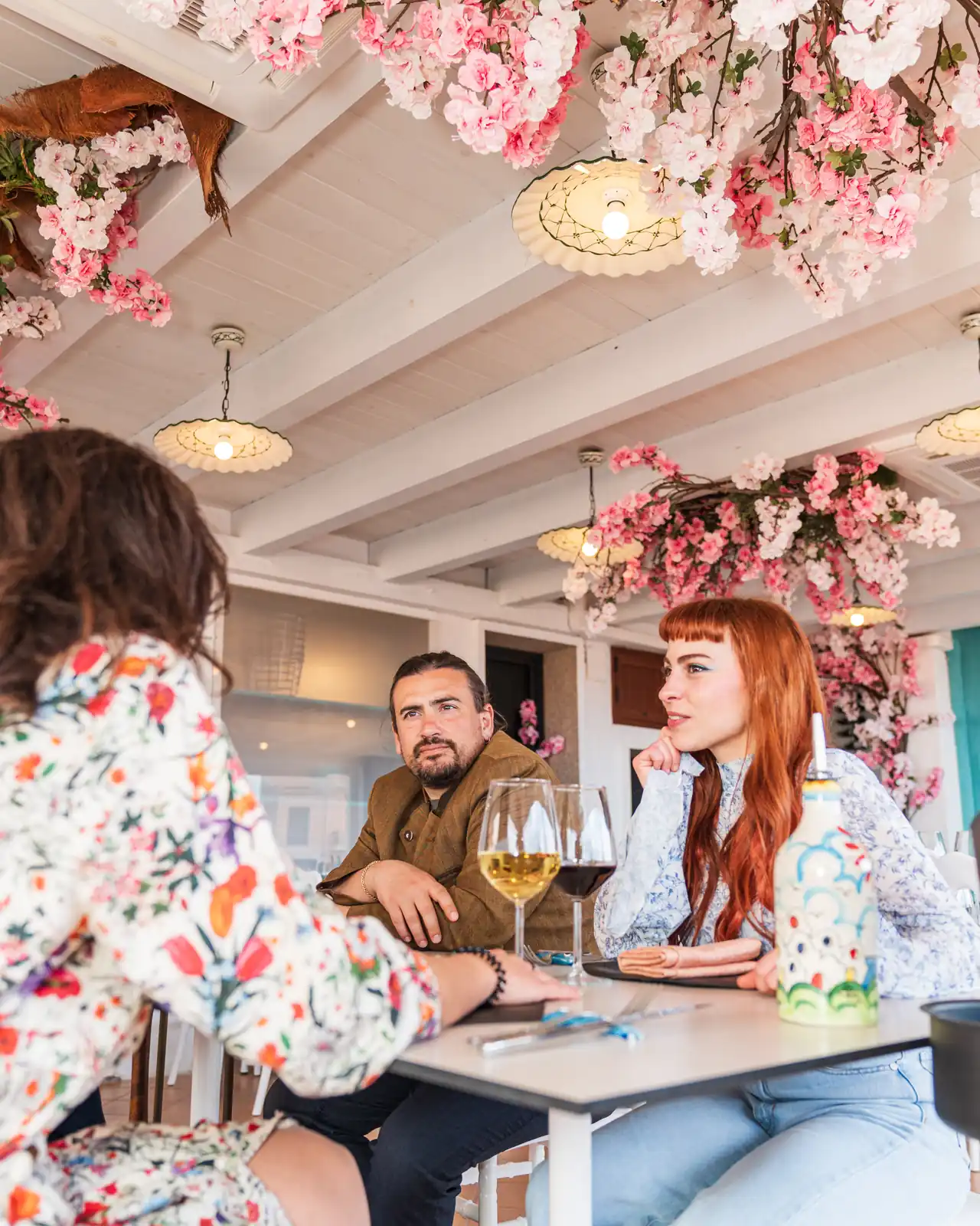Due ospiti a tavola sotto i fiori, con un calice di vino
