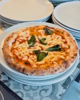 Una pizza margherita appena sfornata, sulla pila dei piatti in cucina