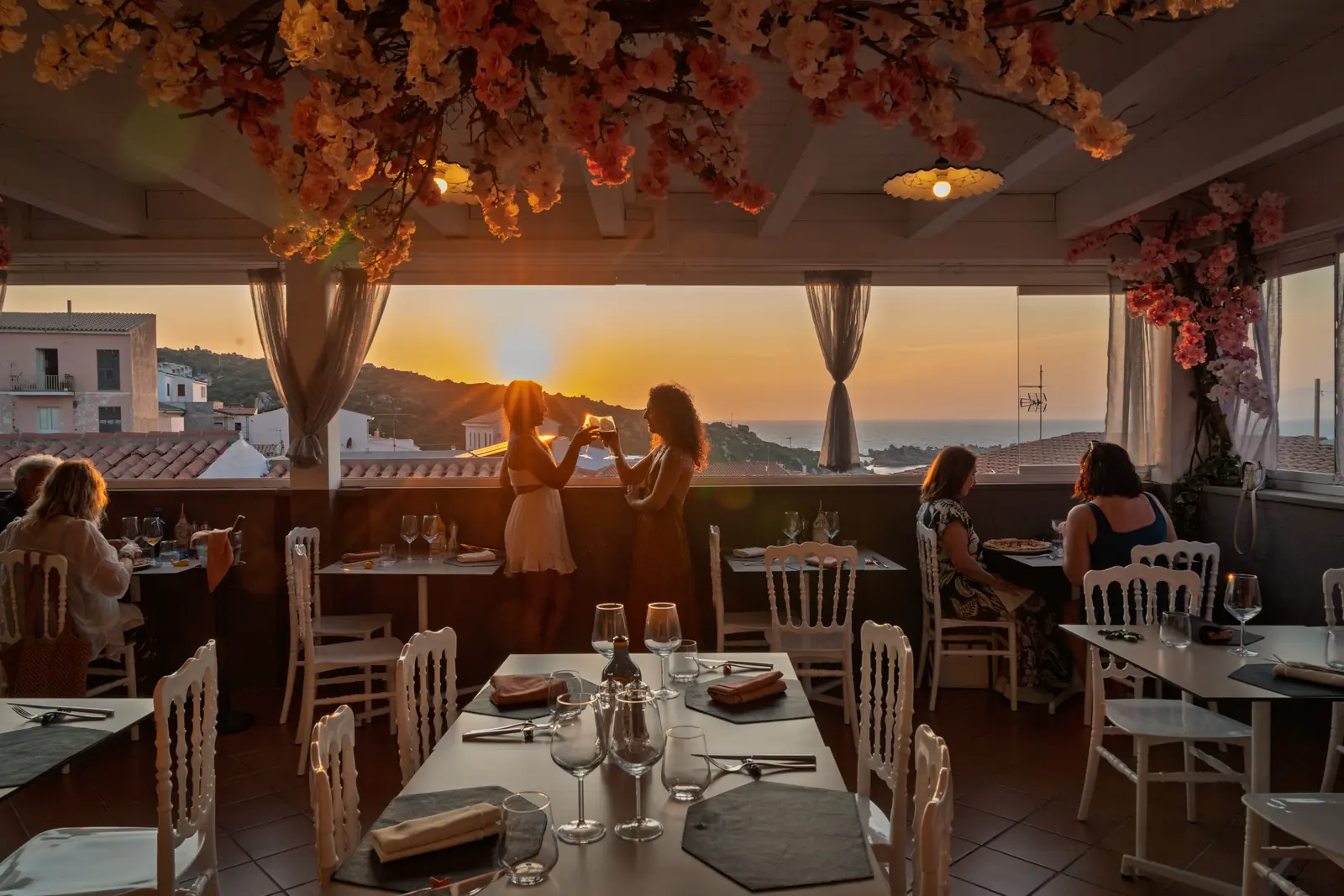 La terrazza al tramonto con gli ospiti ai tavoli e le tende mosse dal vento
