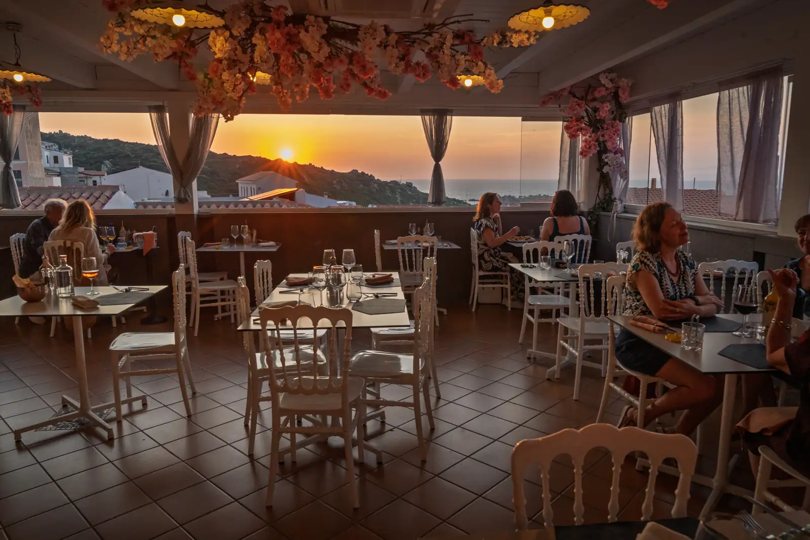 I tavoli della terrazza al tramonto, con gli ospiti seduti e il sole sul mare